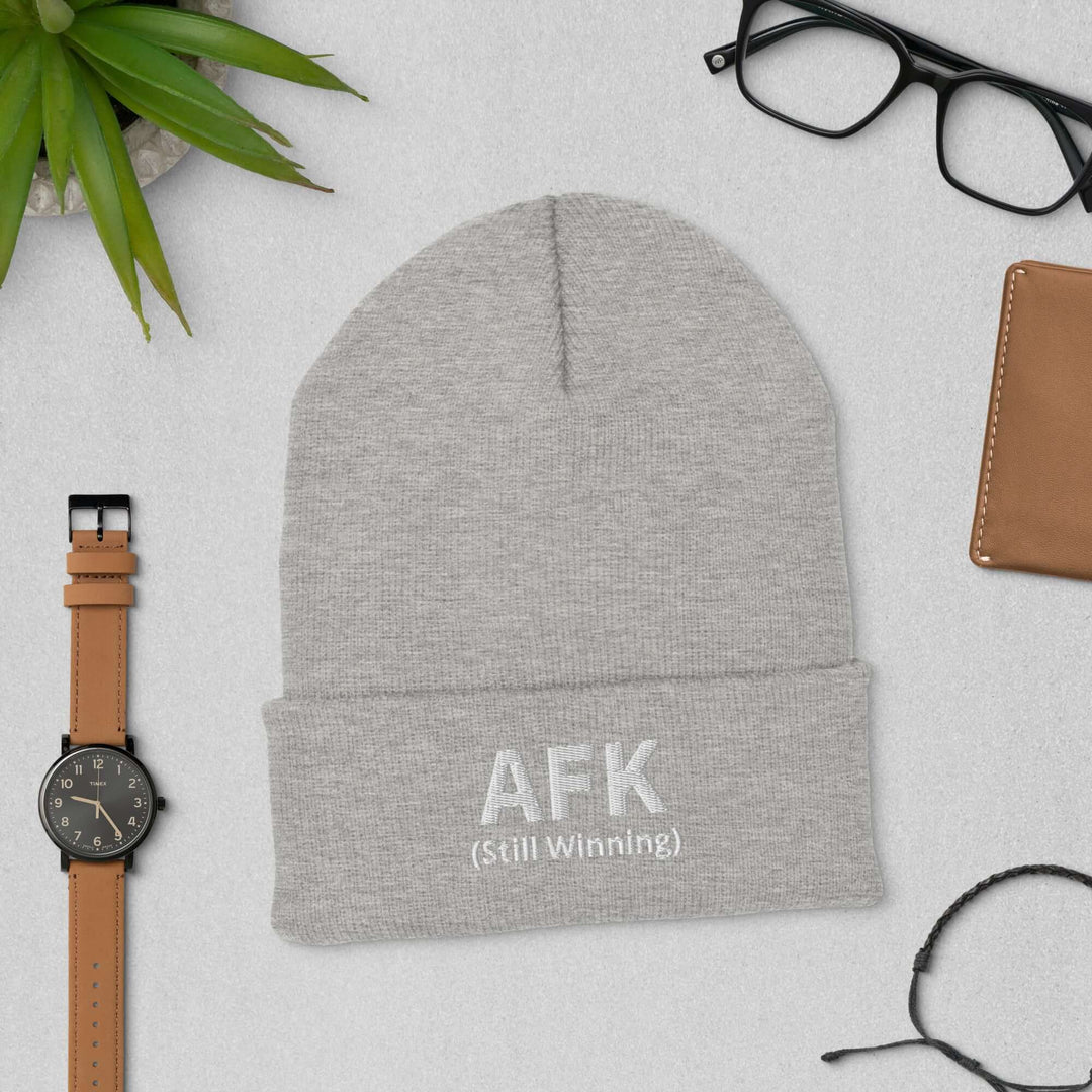 AFK cuffed beanie displayed with accessories like glasses and a watch on a textured surface.