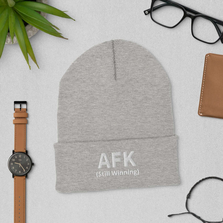 AFK cuffed beanie displayed with accessories like glasses and a watch on a textured surface.